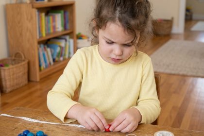 Petite fille de 5 ans qui enfile des perles colorées en bois pour développer sa motricité fine